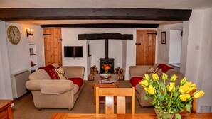 A cozy living room with a fireplace, two sofas, a wooden coffee table, and a vase of yellow flowers. - Cottage in Alcombe near Exmoor Park (Alcombe)