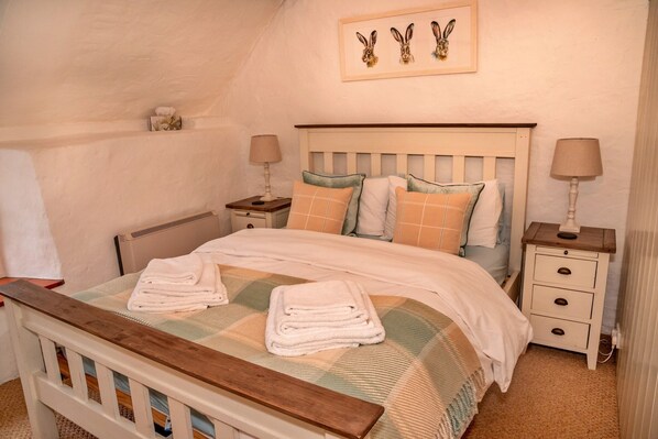 A cozy bedroom with a wooden bed frame, a headboard, a bedside table with a lamp, and a wall-mounted picture.