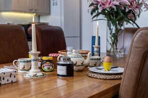A beautifully set dining table features a teapot, marmalade, and a ceramic egg, accompanied by a candle.