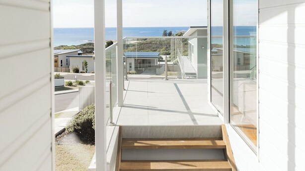 A corridor with a wooden staircase leading to a balcony with a view of the sea and other buildings.