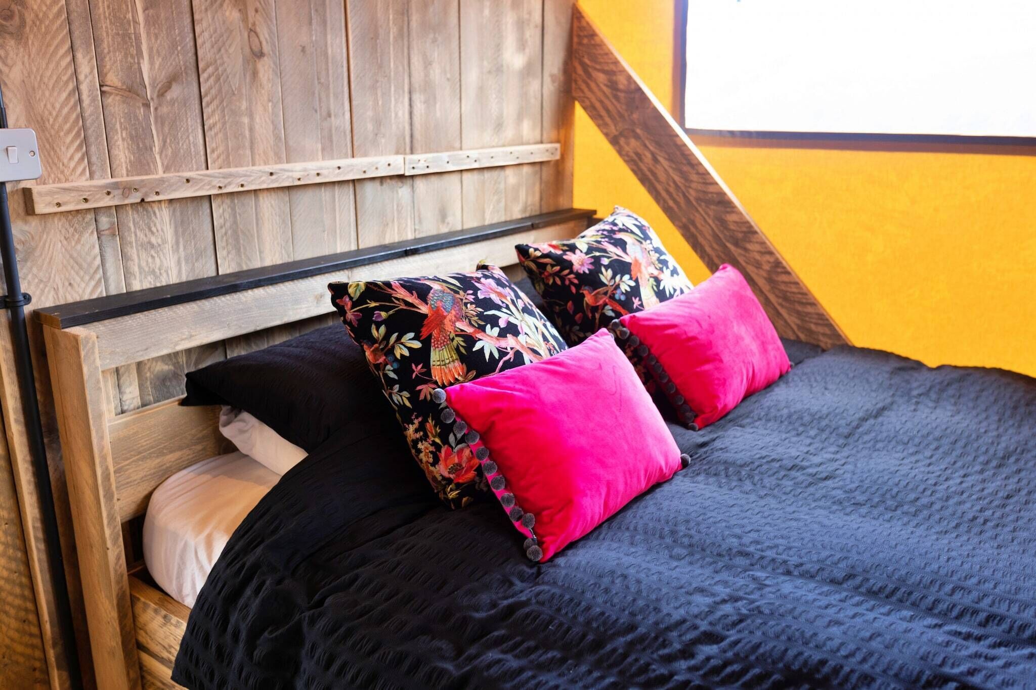 Un lit avec une tête de lit en bois, une literie noire et deux coussins à motifs floraux.