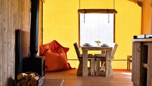 Une pièce chaleureuse avec un plancher en bois, une table entourée de chaises, un poêle noir et une fenêtre donnant sur un beau paysage.