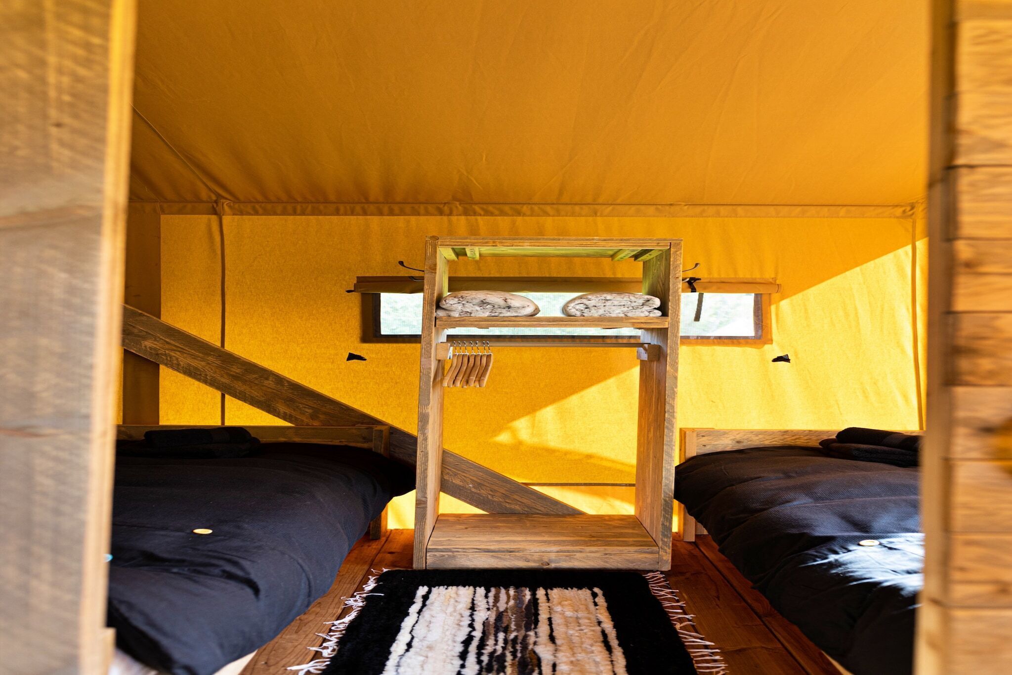 A tent with two beds, a wooden ladder, and a small window.