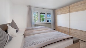 A bedroom with a bed, a window with curtains, a radiator, and a wooden wardrobe.