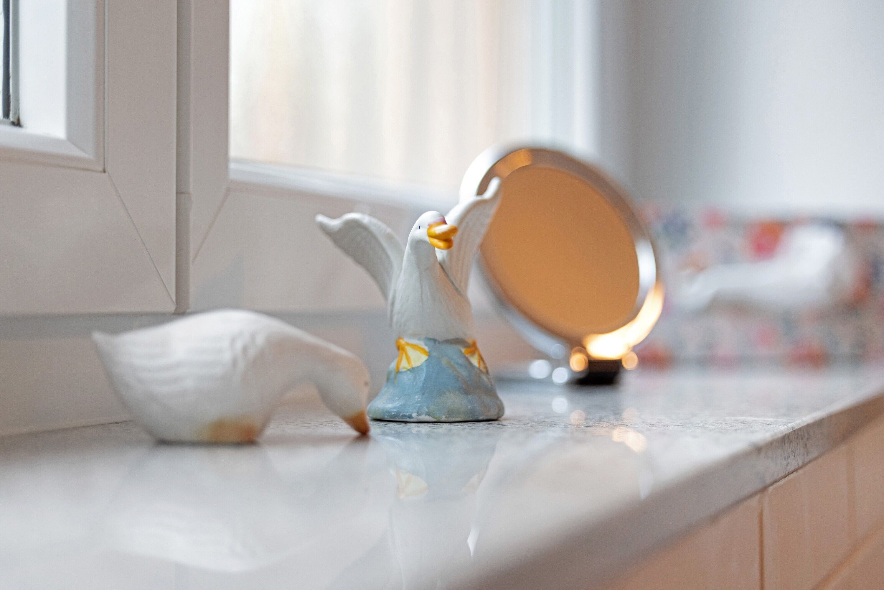 Eine Keramikvogel-Figur auf einer Küchenarbeitsplatte in der Nähe eines Fensters.