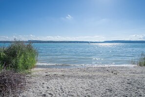 A beach with clear water, a distant sailboat, and a hilly landscape.