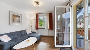 A modern living room with a sofa, a coffee table, a framed picture, a floor lamp, and a sliding glass door leading to a balcony. - Apartment 'Weinberg' with Balcony (Meersburg)