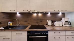 A kitchen with wooden cabinets, a built-in oven, a stovetop, a sink, and a coffee maker. - Apartment 'Weinberg' with Balcony (Meersburg)