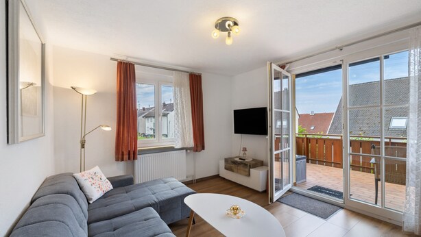 A modern living room with a grey sectional sofa, a white coffee table, a flat-screen TV, and a sliding glass door leading to a balcony. - Apartment 'Weinberg' with Balcony (Meersburg)