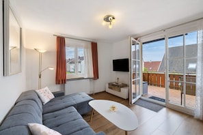 A modern living room with a grey sectional sofa, a white coffee table, a flat-screen TV, and a sliding glass door leading to a balcony. - Apartment 'Weinberg' with Balcony (Meersburg)