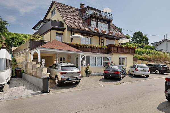 Une maison à deux étages avec un balcon, des voitures garées et une statue dans l’allée.