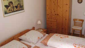 Een slaapkamer met een houten garderobe, een bed met bloemenbedrukking, een stoel en een schilderij aan de muur.