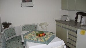 Een kleine keuken met een tafel voor twee personen, een stoel en een potplant.