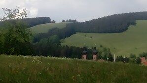 Een landelijk landschap met glooiende heuvels, een kerk en enkele gebouwen.