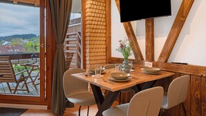 Un coin repas avec une table en bois, des chaises, un téléviseur fixé au mur et une vue sur l’extérieur.