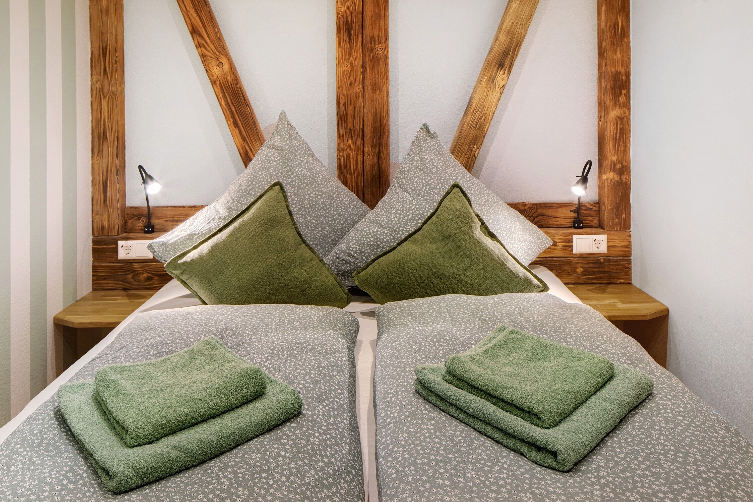 Ein ordentlich bezogenes Bett mit grünen Handtüchern, einem Holzkopfstück und Nachttischlampen.