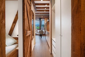 A narrow hallway with wooden beams, a bed with a pillow, and a dining area with a table and chairs. - Holiday Apartment 'Am Bärenhof' with Mountain View, Sauna, Balcony and Wi-Fi (Titisee-Neustadt)
