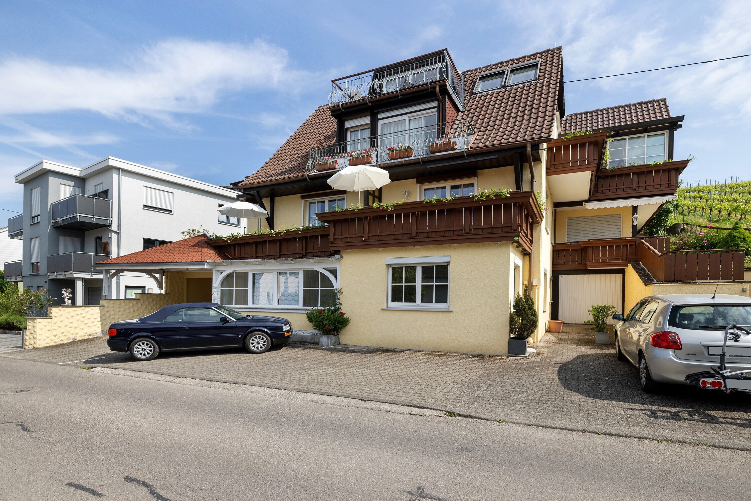 A two-story house with a car parked in the driveway, a balcony with plants, and a garage.