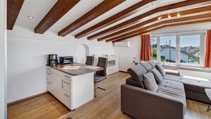 A modern kitchen with wooden beams, a dining area with a sofa, and a view of buildings outside. - Apartment 'Seeblick' with balcony, mountain and lake view (Meersburg)
