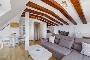 Un intérieur moderne avec un plafond en bois, un canapé gris, une table blanche et un coin cuisine.