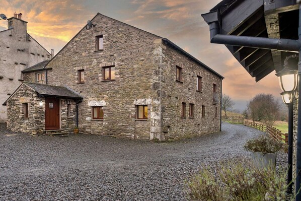 A stone building with a sloped roof, a wooden door, and multiple windows. - Cottage in Lake District with Sauna & Views (Bretherdale)