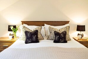 A neatly made bed with patterned pillows, a vase with flowers, and two bedside lamps on wooden nightstands. - Cottage in Lake District with Sauna & Views (Bretherdale)