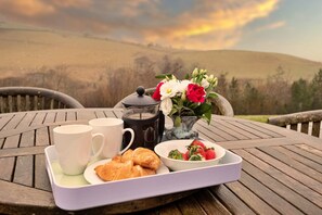 A wooden table with a tray containing a coffee pot, two white cups, a plate with croissants, a bowl of strawberries, and a vase with flowers. - Cottage in Lake District with Sauna & Views (Bretherdale)