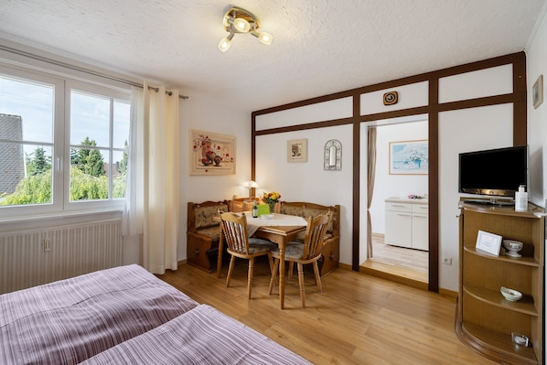A room with a bed, a dining table with chairs, a TV, and a view of the outdoors.