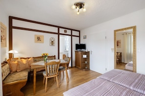 A room with a bed, a sofa, a dining table with chairs, a television, and a cabinet.