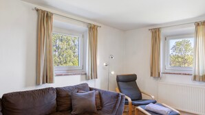 A living room with a sofa, a chair, and a table. There are windows with curtains, a radiator, and a lamp. - Holiday Home 'Ferienhaus Kreuzbergblick' with Mountain View, Private Terrace and Wi-Fi (Hohenau)