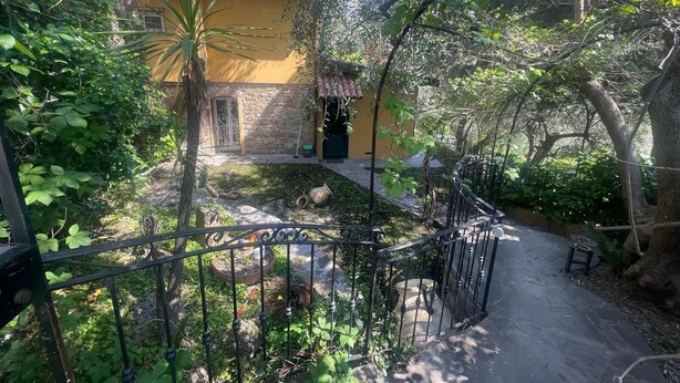 A courtyard with a yellow building, stone walls, and a metal fence.