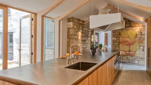 Une cuisine moderne dotée d’un grand îlot central, d’un mur en pierre et de poutres en bois.