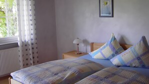 Un dormitorio con dos camas, una mesita de noche con lámpara, una ventana con cortinas y un cuadro en la pared.