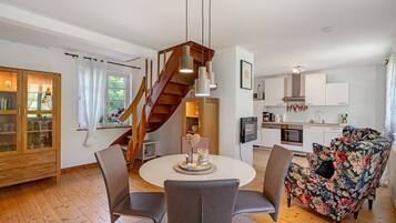 Eine moderne Küche mit weißen Schränken, einer Holztreppe, einem Essbereich mit rundem Tisch und Stühlen sowie einem Blumensofa.