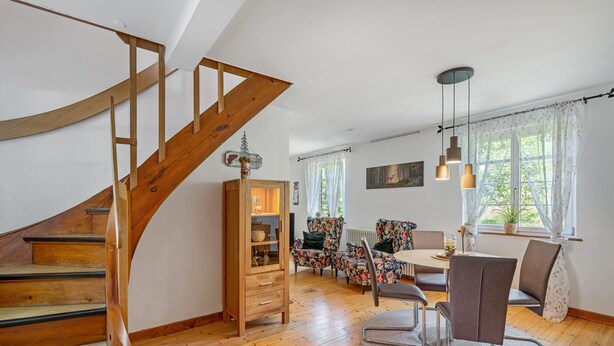 Un escalier en bois mène à un espace repas comprenant une table et des chaises, un radiateur et une fenêtre avec des rideaux.