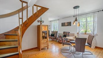 Eine Holztreppe führt zu einem Essbereich mit Tisch und Stühlen, einem Heizkörper und einem Fenster mit Vorhängen.
