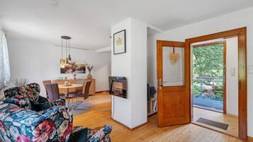 Ein Wohnzimmer mit einer Couch, einem Esstisch, Stühlen, einem Fernseher und einer Holztür, die nach draußen führt.