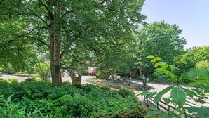 Un jardin luxuriant, avec une grande variété d’arbres et d’arbustes, un chemin pavé et un bâtiment en arrière-plan.