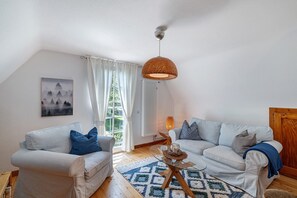 Una sala de estar con un sofá blanco, un sofá azul, un tapete estampado, una lámpara colgante y un cuadro en la pared.
