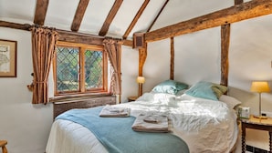 Un dormitorio con una cama grande, vigas de madera, un ventanal con cortinas y una mesita de noche con lámpara.