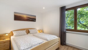 Une chambre à coucher avec un lit, des tables de chevet, une fenêtre donnant sur des arbres et un tableau accroché au mur.