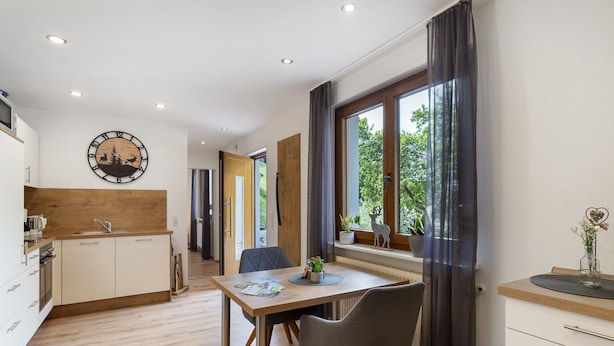 Une cuisine moderne avec un plan de travail en bois, un coin repas comprenant une table et des chaises, et une grande fenêtre agrémentée de rideaux.