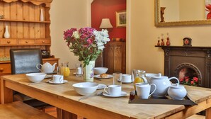 Una mesa de comedor dispuesta con vajilla blanca, un florero y una chimenea al fondo.