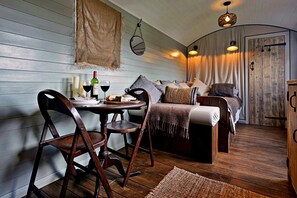 A cozy room with a wooden dining table, chairs, and a bed with a headboard. - Shepherd’s Hut on Llŷn Peninsula by Private Lake (Pwllheli)