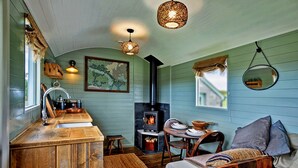 A cozy room with a wooden bar, a fireplace, a dining table, and a comfortable seating area. - Shepherd’s Hut on Llŷn Peninsula by Private Lake (Pwllheli)