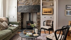 A cozy living room with a stone fireplace, a green sofa, a black armchair, and a coffee table with books and cookies.