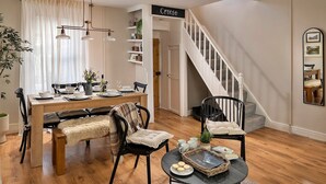 A dining area with a wooden table, chairs, and a bench. There is a staircase with a white railing leading to another room.