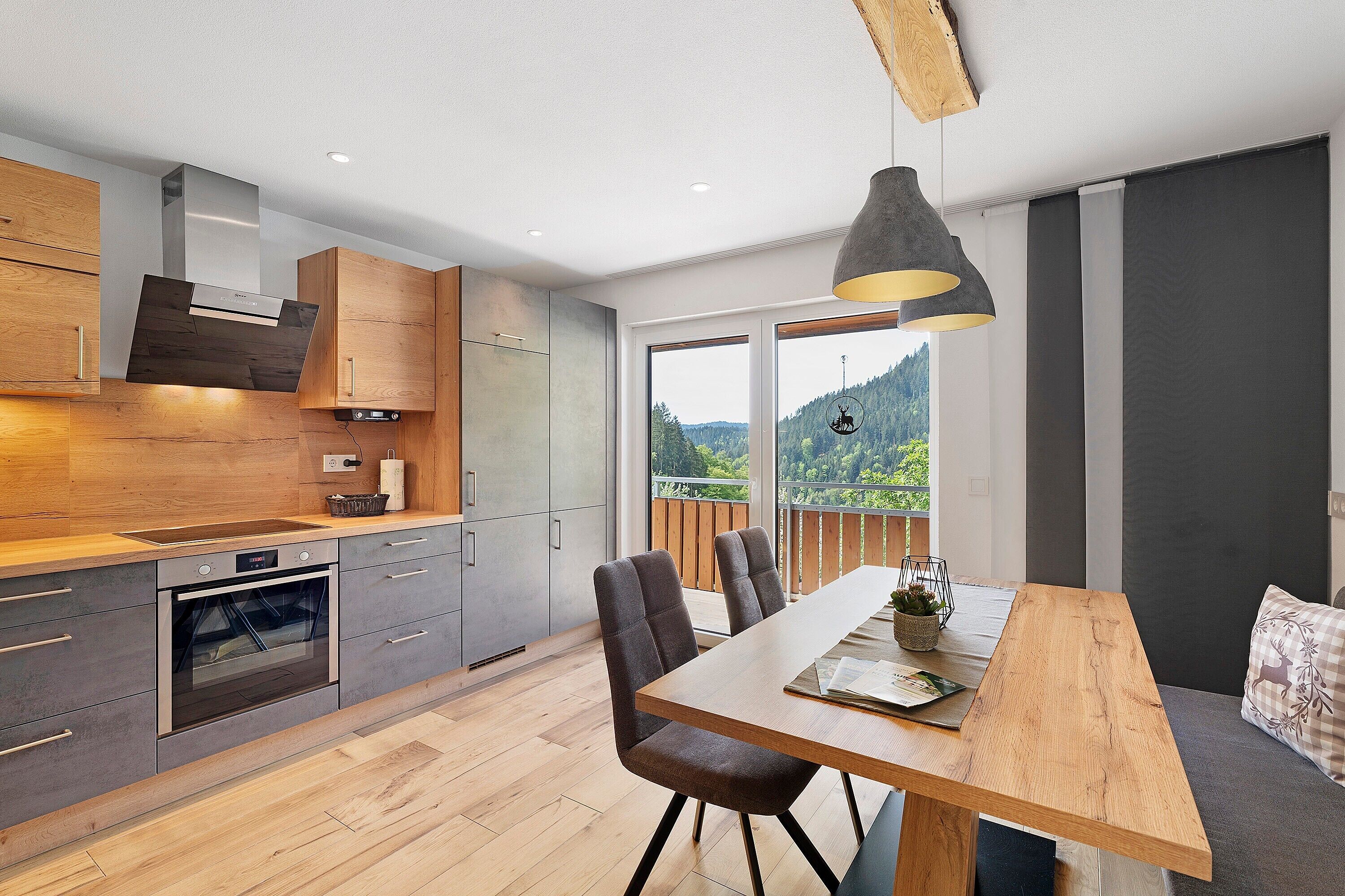 A modern kitchen with a built-in oven, wooden cabinets, and a dining area with a table and chairs. - Holderstanzenhof: Apartment 'Talblick' with Mountain View, Private Balcony and Wi-Fi (Bad Peterstal-Griesbach)