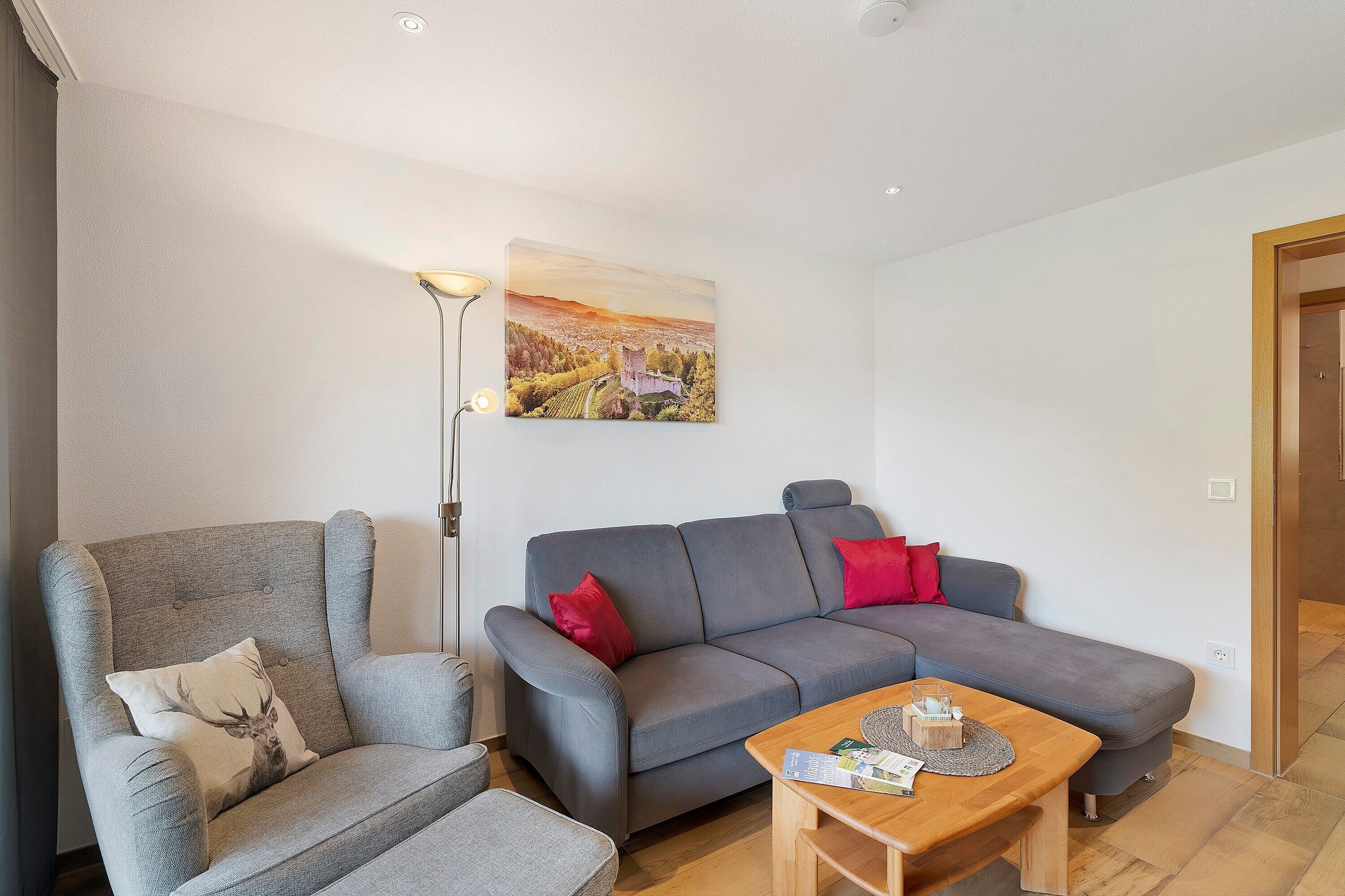 Un salon moderne avec un canapé gris, un fauteuil assorti, une table basse en bois et un tableau accroché au mur.