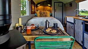 A cozy interior with a bed, a table with breakfast items, a sink, and a window with a view of greenery. - Shepherd's Hut on Llŷn Peninsula, Near Snowdonia (Pwllheli)